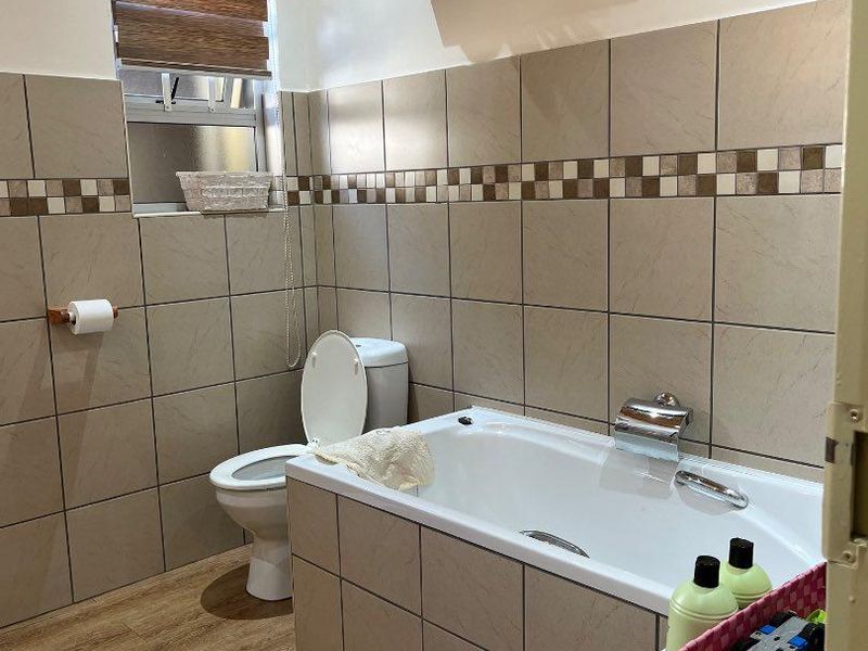 A functional bathroom featuring tiled walls, a built-in bathtub, a toilet, and a timber ceiling with wood-look flooring.