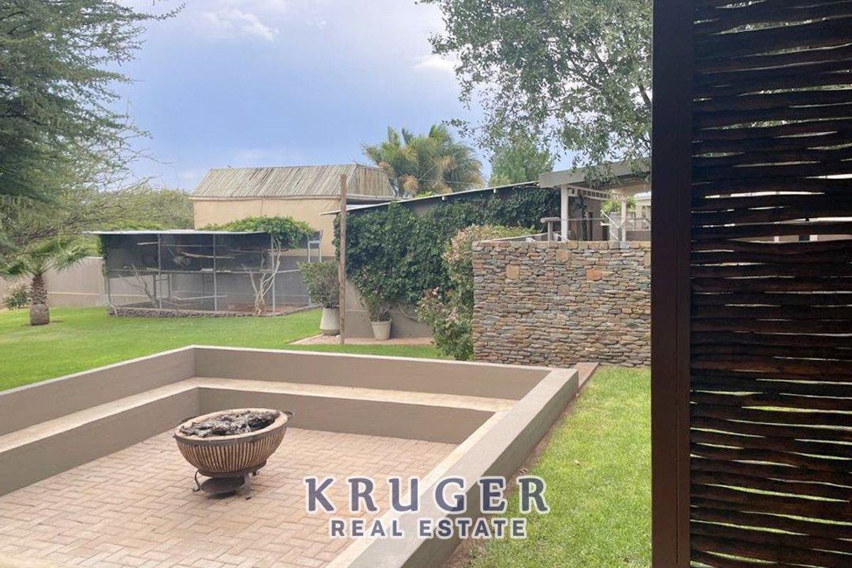 A landscaped rear garden featuring a sunken paved patio area with a fire pit, stone feature wall, and established lawn.