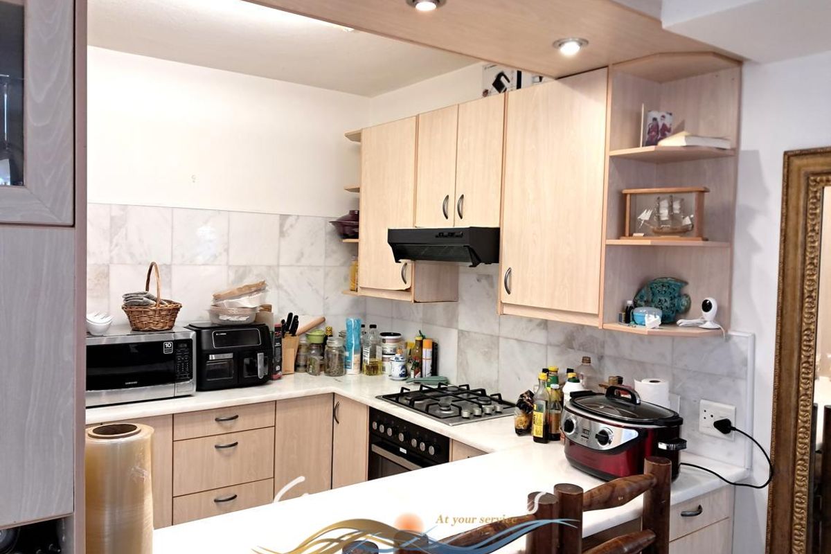 A functional kitchen featuring light wood-finish cabinetry, a gas hob with extractor fan, and marble-look tiled backsplash with ample counter space.