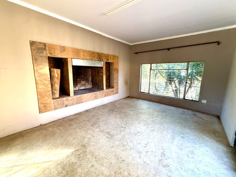 An empty living room featuring a built-in stone fireplace, large window with security bars, and concrete flooring, offering a blank canvas for renovation.