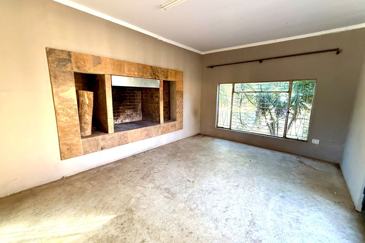 An empty living room featuring a built-in stone fireplace, large window with security bars, and concrete flooring, offering a blank canvas for renovation.