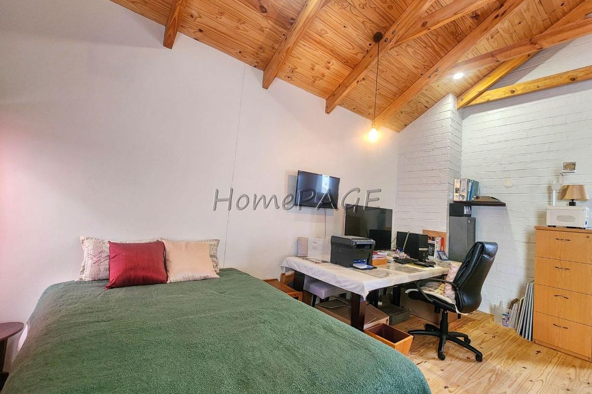 A bedroom featuring exposed timber vaulted ceilings, light wood flooring, and a painted brick feature wall.