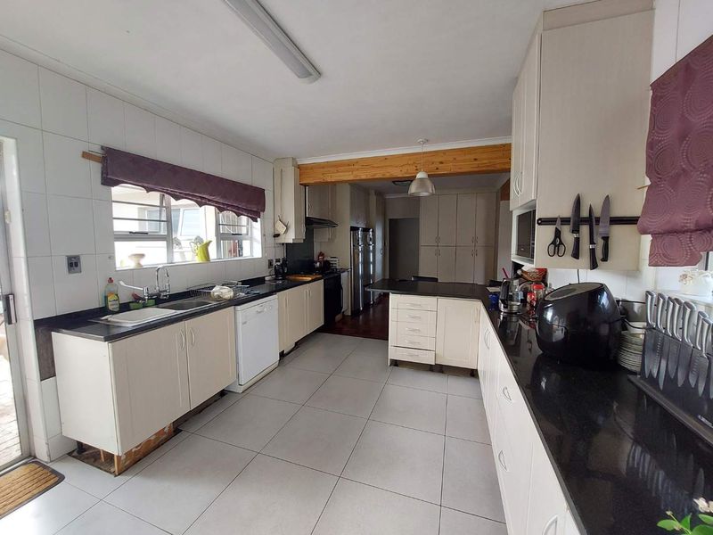 Spacious kitchen featuring extensive built-in cabinetry, granite countertops, tiled flooring, and an exposed timber beam, offering a functional layout with ample storage space.