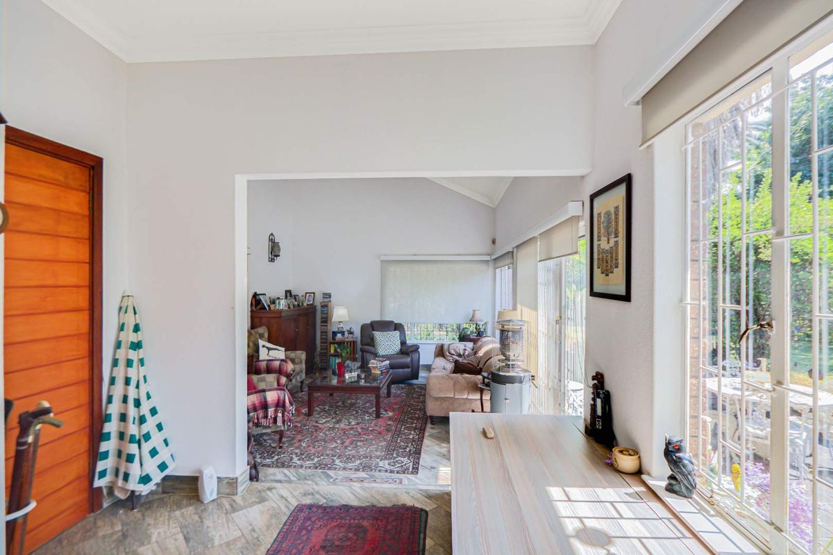 A bright living area featuring tiled flooring, large windows with security bars, and direct access to the outdoor space.