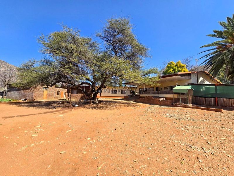 Rear view of the small holding property featuring a large mature tree, brick outbuilding, and a covered patio area.