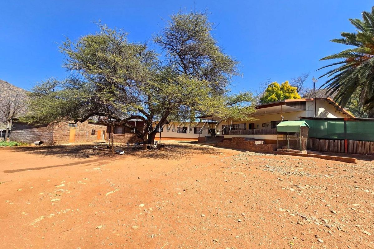 Rear view of the small holding property featuring a large mature tree, brick outbuilding, and a covered patio area.