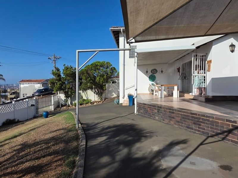 A covered patio area featuring tiled flooring, a brick retaining wall, and a shade sail, providing a functional outdoor space for relaxation.