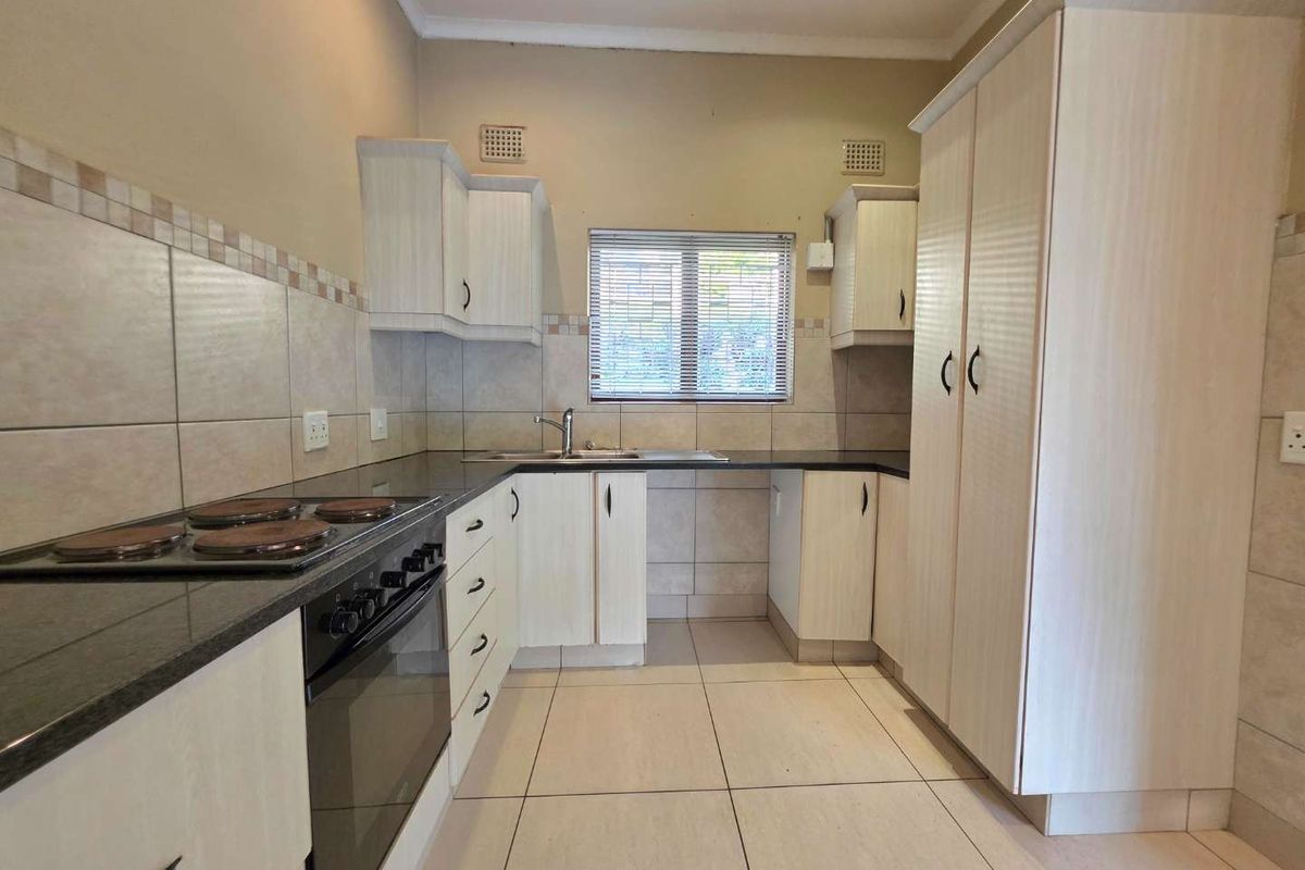 A functional kitchen featuring light-toned cabinetry, dark granite countertops, a built-in oven with electric hob, and tiled flooring throughout.