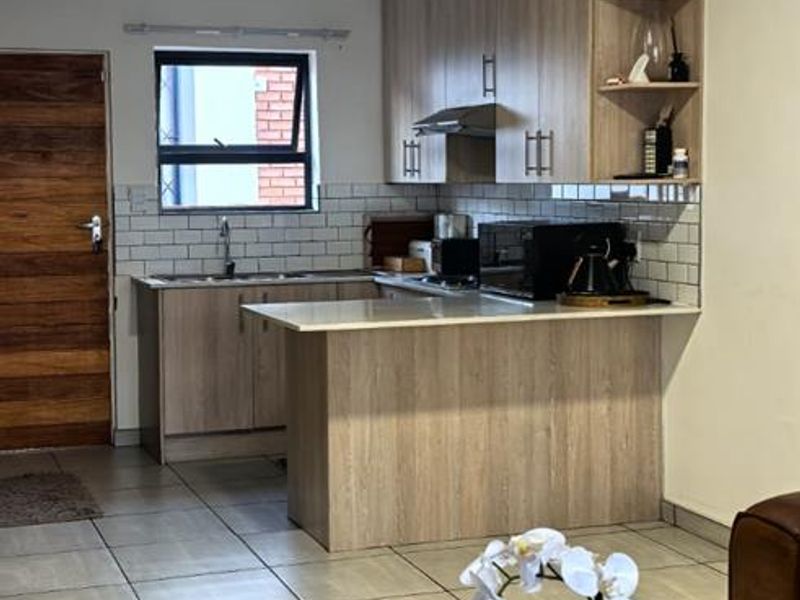 Open plan kitchen featuring light wood cabinetry, a breakfast bar island, subway tile backsplash, and tiled flooring, seamlessly integrated with the living area.