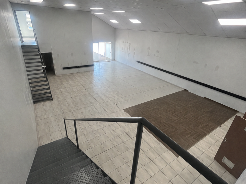 Spacious open-plan commercial area featuring a mix of tiled and parquet flooring, suspended ceilings with recessed lighting, and a metal staircase.
