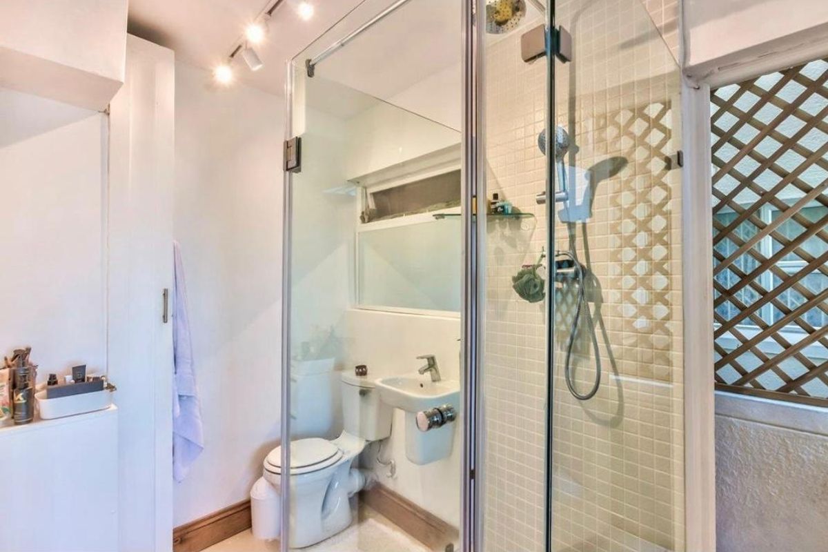 Compact bathroom featuring a glass-enclosed shower, wall-mounted basin, toilet, and mosaic tile finishes with integrated lighting.