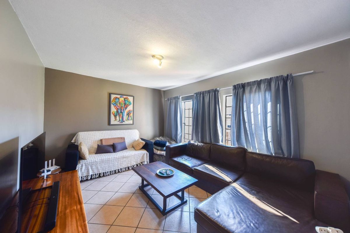 A comfortable living room featuring tiled flooring and large windows with curtain tracks, providing a functional and well-lit space for relaxation.