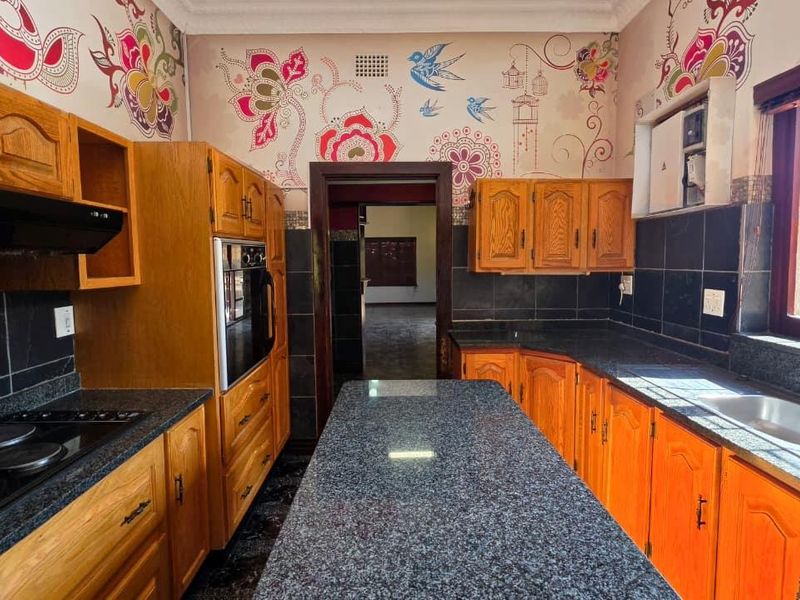 A functional kitchen featuring wooden cabinetry, granite countertops, a built-in oven, and an electric hob, offering a solid foundation for modern renovation.