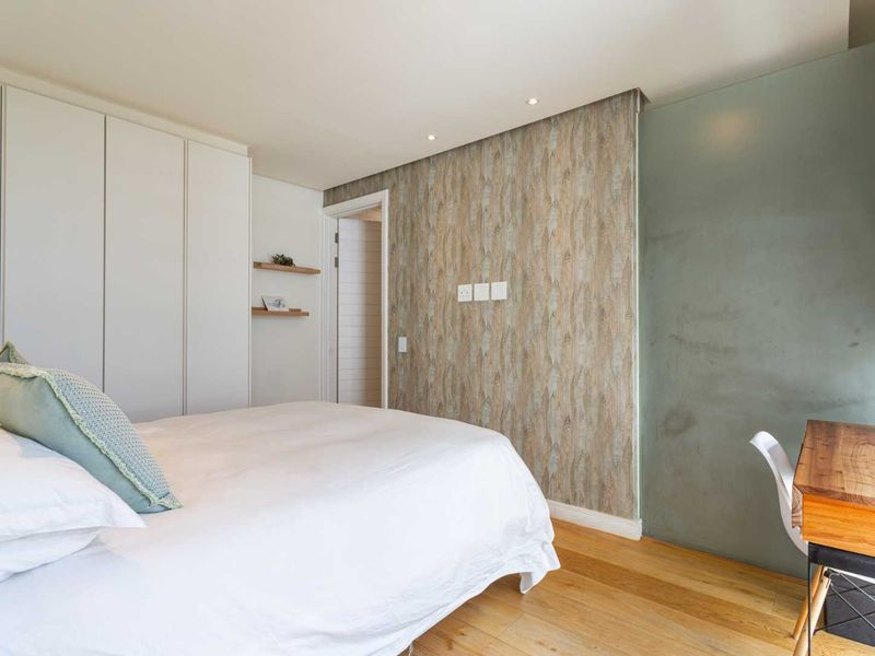 A well-maintained bedroom featuring built-in wardrobes, timber flooring, recessed lighting, and a modern frosted glass partition wall.
