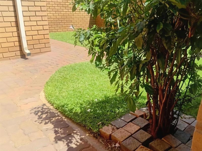 A well-maintained garden area featuring neat brick paving, a manicured lawn, and a brick boundary wall with an integrated downpipe.