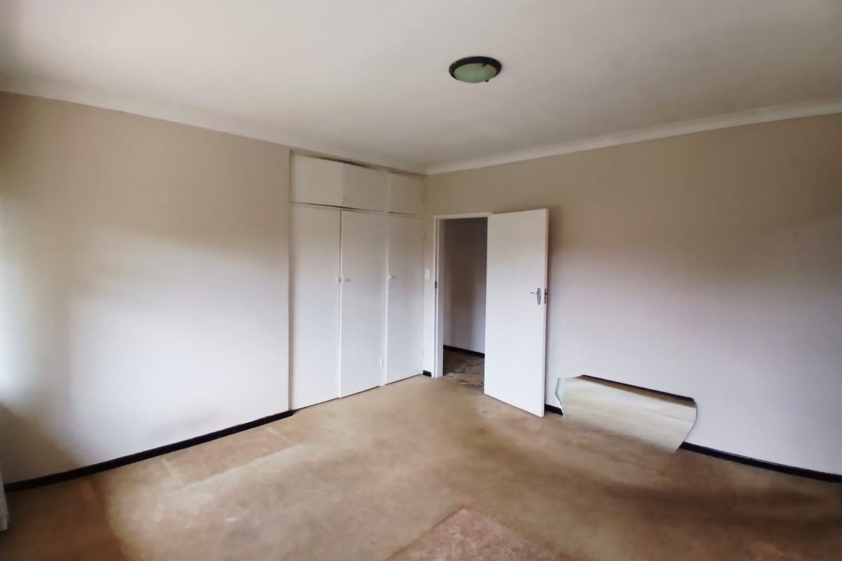 An empty bedroom featuring built-in cupboards, coving, and a flush mount ceiling light, requiring flooring and wall repairs.