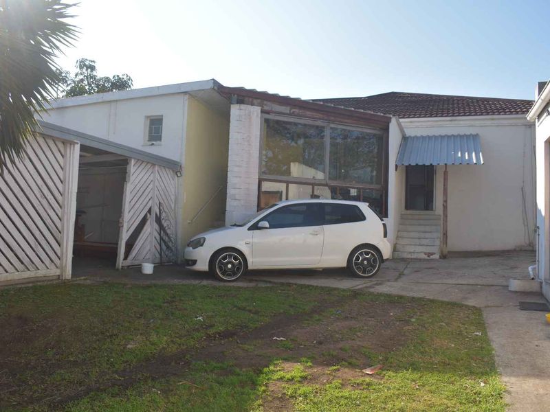 Rear exterior view of the property featuring a carport, concrete driveway, and access steps leading to the main building structure.