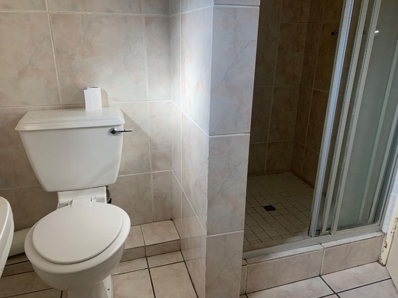 A functional bathroom featuring a standard toilet and a separate shower enclosure with tiled finishes throughout.