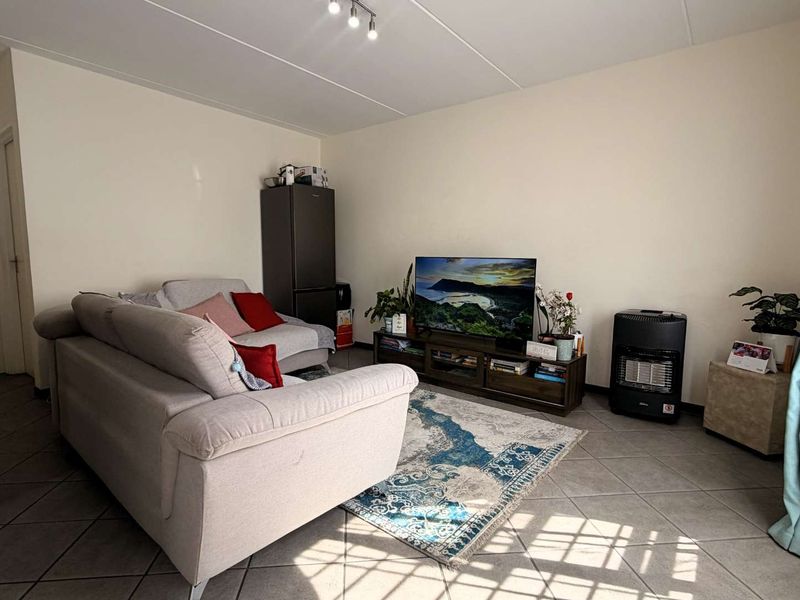 A functional living room featuring neutral tiled flooring and ceiling track lighting, providing a versatile space for relaxation and entertainment.