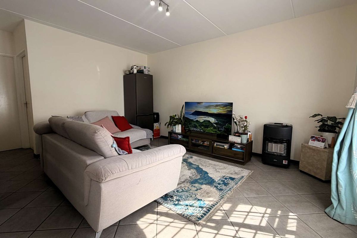 A functional living room featuring neutral tiled flooring and ceiling track lighting, providing a versatile space for relaxation and entertainment.