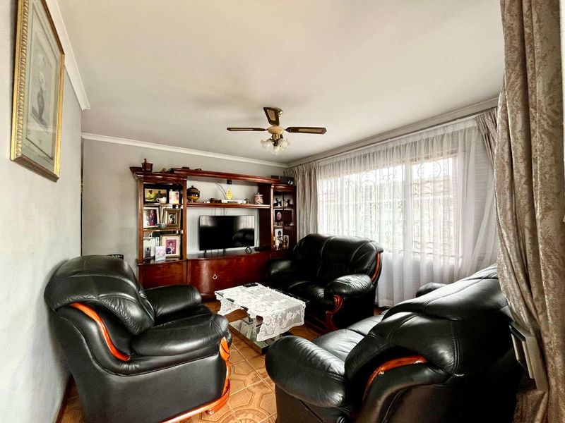 A comfortable living room featuring tiled flooring, a ceiling fan, and a large window with security bars, providing a functional and well-lit space.