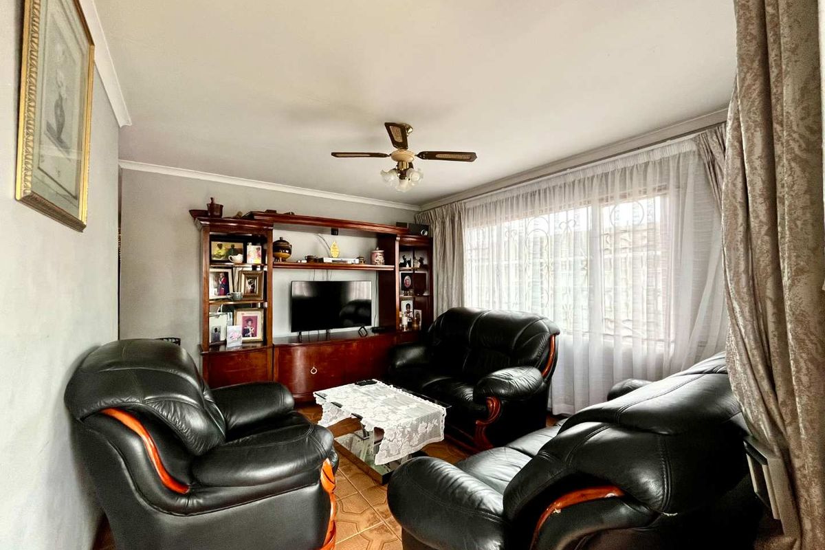 A comfortable living room featuring tiled flooring, a ceiling fan, and a large window with security bars, providing a functional and well-lit space.