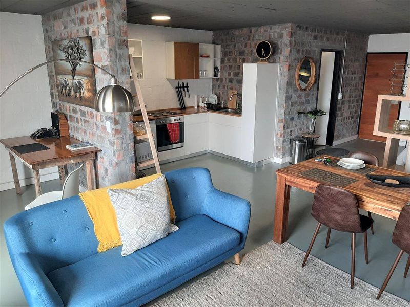 Open-plan living area featuring exposed brick walls, polished concrete floors, and a modern kitchen with integrated appliances.