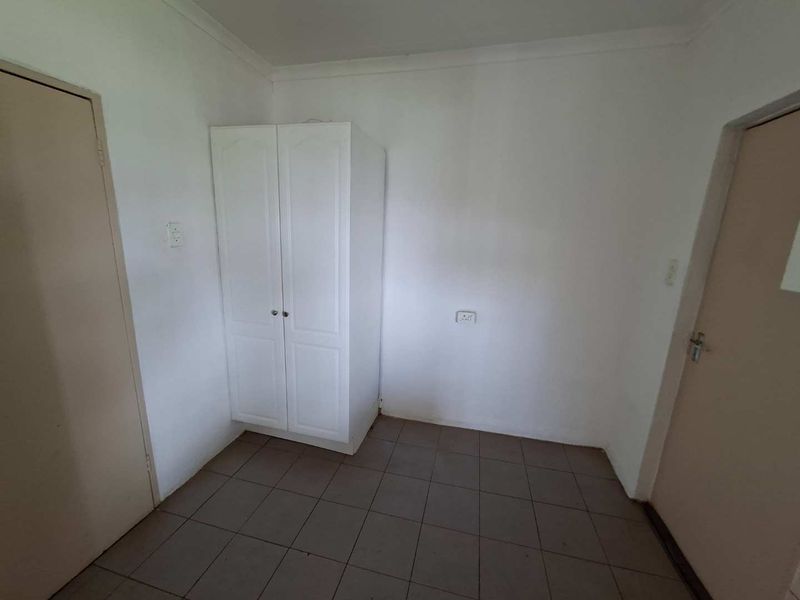 A simple bedroom featuring tiled flooring and a built-in wardrobe, offering a blank canvas for potential interior updates.