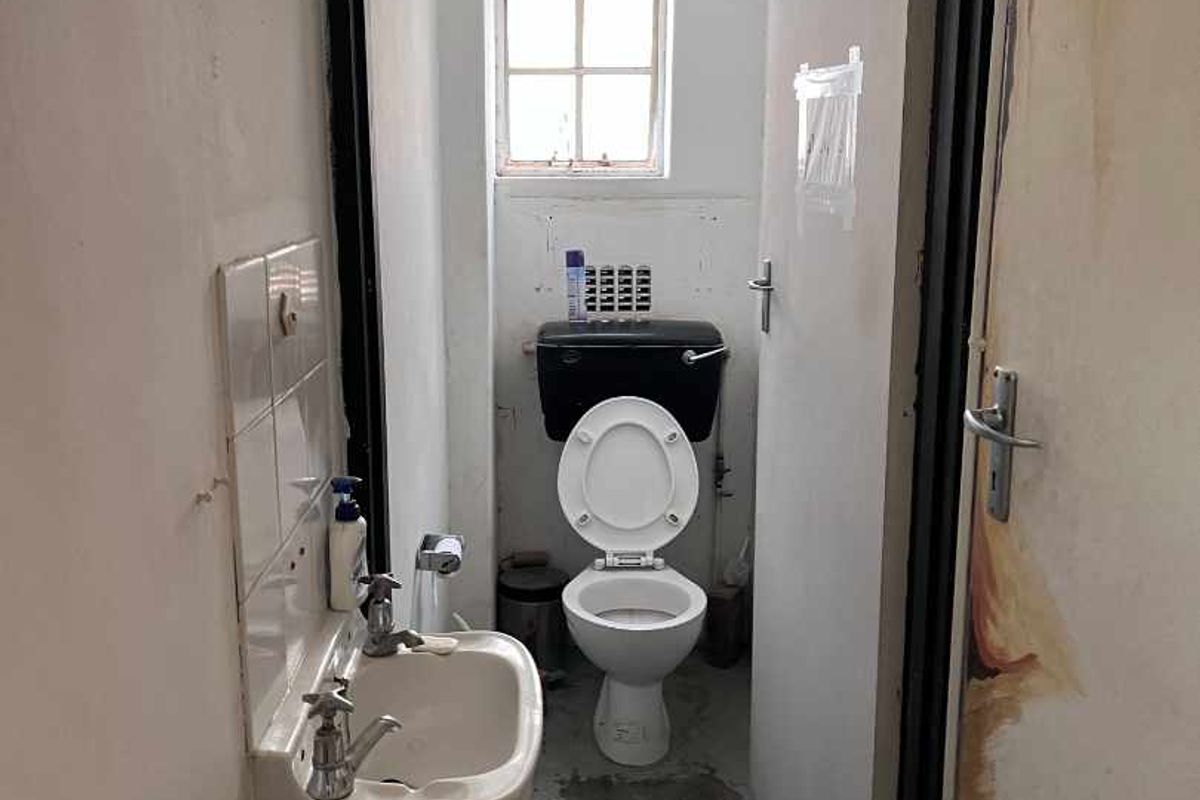 A small, dated bathroom featuring a wall-mounted basin and toilet, requiring significant cosmetic updates and repairs to the flooring and wall finishes.