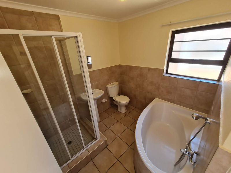 A functional bathroom featuring a corner bathtub, separate shower enclosure, pedestal basin, and toilet with neutral tiled finishes.