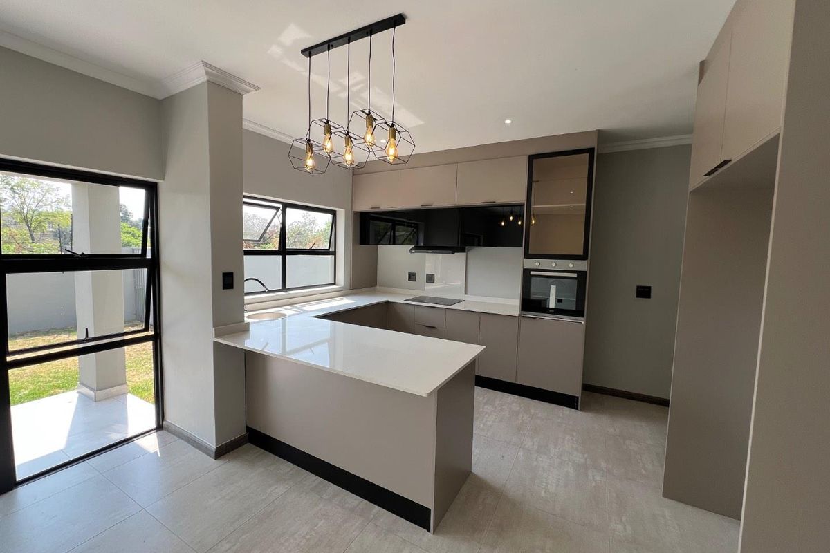Modern kitchen featuring sleek cabinetry, stone countertops, a breakfast bar, built-in oven, and large windows providing natural light and garden access.