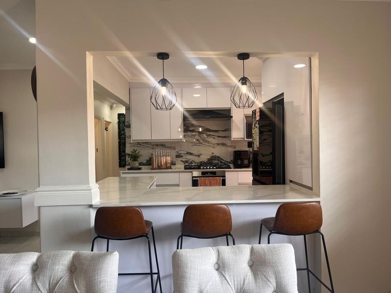 Modern kitchen featuring white cabinetry, marble-look splashback, gas hob, and a convenient breakfast bar pass-through to the living area.