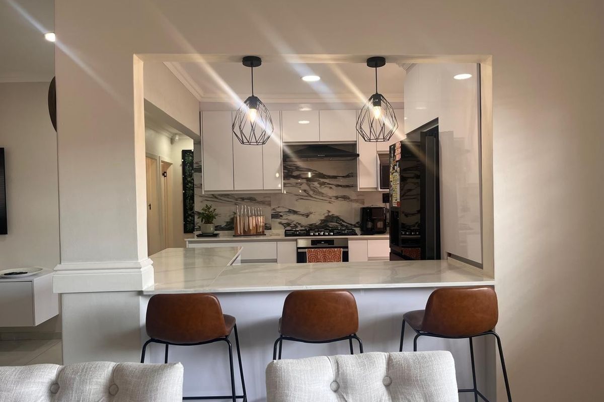 Modern kitchen featuring white cabinetry, marble-look splashback, gas hob, and a convenient breakfast bar pass-through to the living area.