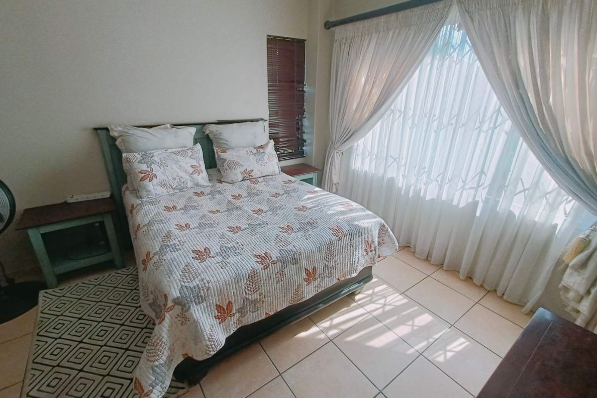 A functional bedroom featuring tiled flooring, a security gate on the window, and natural light through large curtains.
