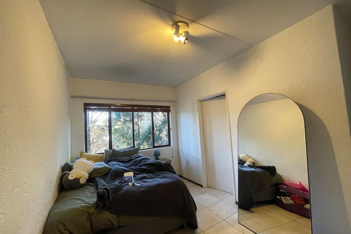 A bedroom featuring tiled flooring, a large window with blinds, and a ceiling-mounted light fixture.