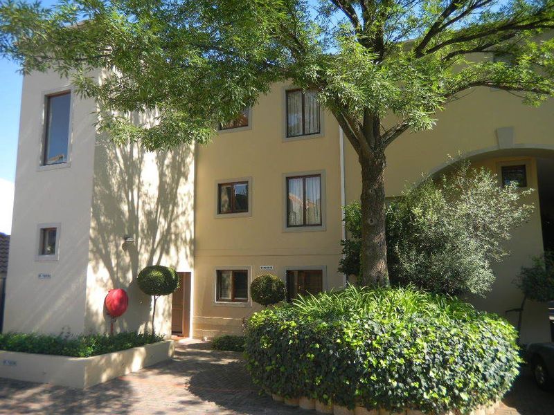 Front elevation of a multi-story apartment building featuring paved driveway access, established trees, and landscaped garden beds.