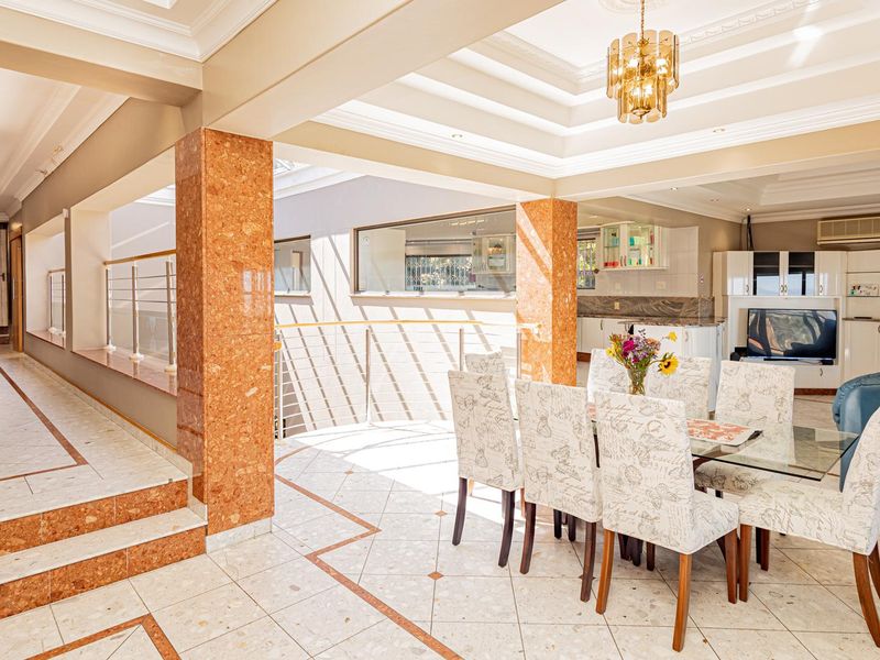 Spacious open-plan living and dining area featuring elegant marble-clad columns, a sophisticated tray ceiling with recessed lighting, and high-quality tiled flooring throughout.
