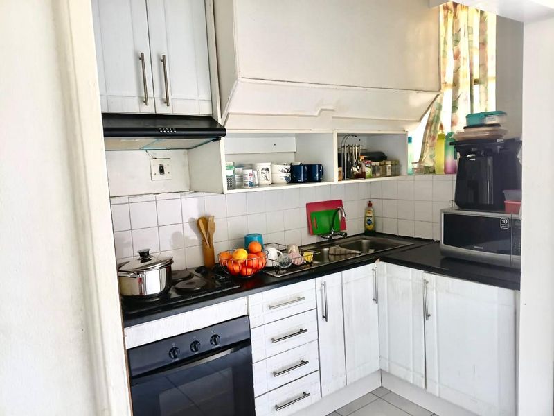 Compact kitchen featuring white built-in cabinetry, dark countertops, a stainless steel sink, and integrated oven with hob and extractor fan.
