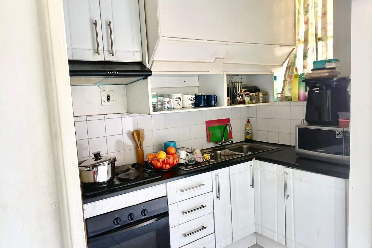 Compact kitchen featuring white built-in cabinetry, dark countertops, a stainless steel sink, and integrated oven with hob and extractor fan.