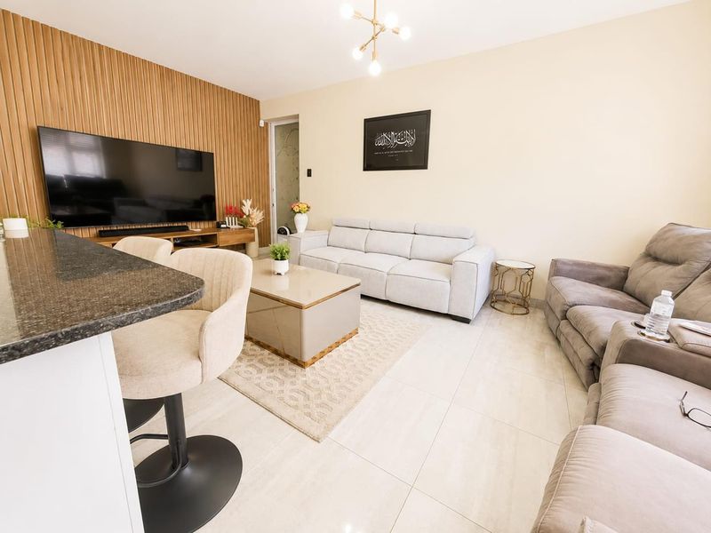 A well-maintained open-plan living area featuring a stylish slatted wood accent wall, neutral tiled flooring, and a granite breakfast bar.