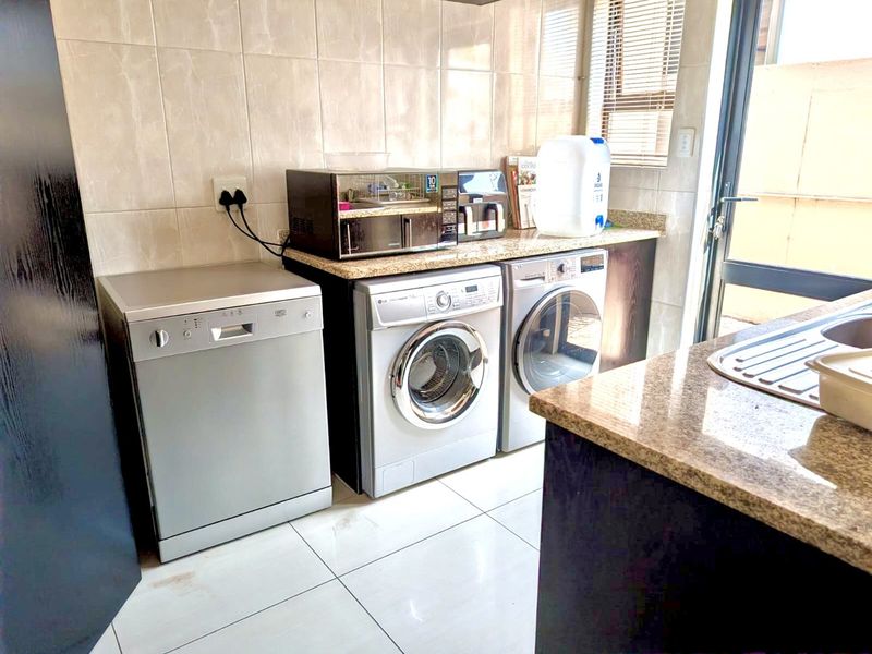 A functional laundry area featuring granite countertops, tiled splashbacks, tiled flooring, and built-in cabinetry with a stainless steel sink.