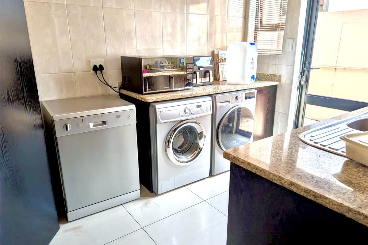 A functional laundry area featuring granite countertops, tiled splashbacks, tiled flooring, and built-in cabinetry with a stainless steel sink.