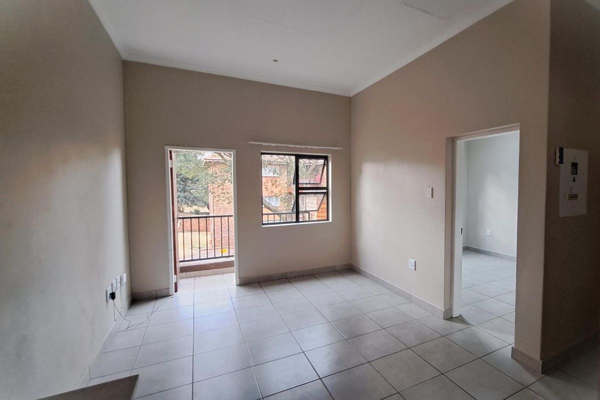 An empty living area featuring neutral tiled flooring, access to a small balcony, and a doorway leading to an adjacent room.