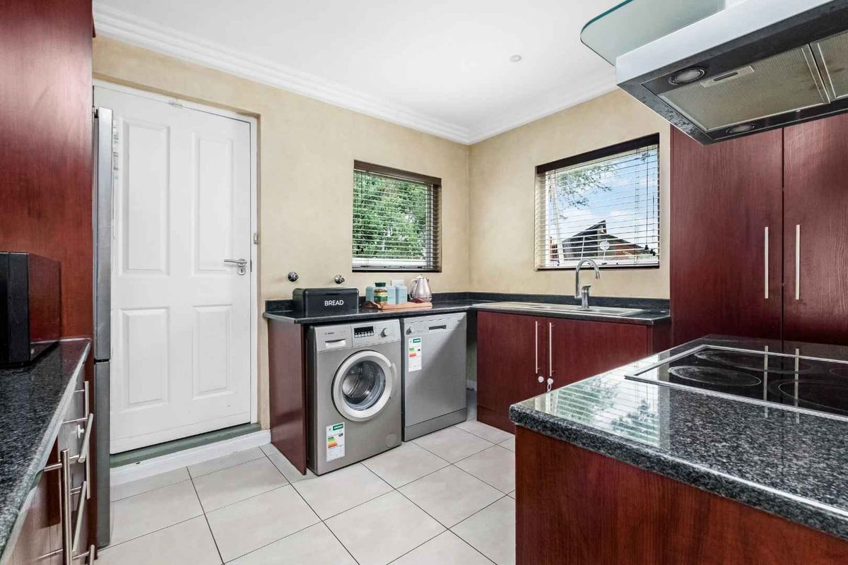 A functional kitchen featuring dark wood cabinetry, granite countertops, tiled flooring, and integrated space for laundry appliances.