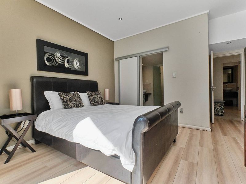 A well-maintained bedroom featuring light laminate flooring, recessed downlighting, and convenient access to an en-suite bathroom through a sliding door.