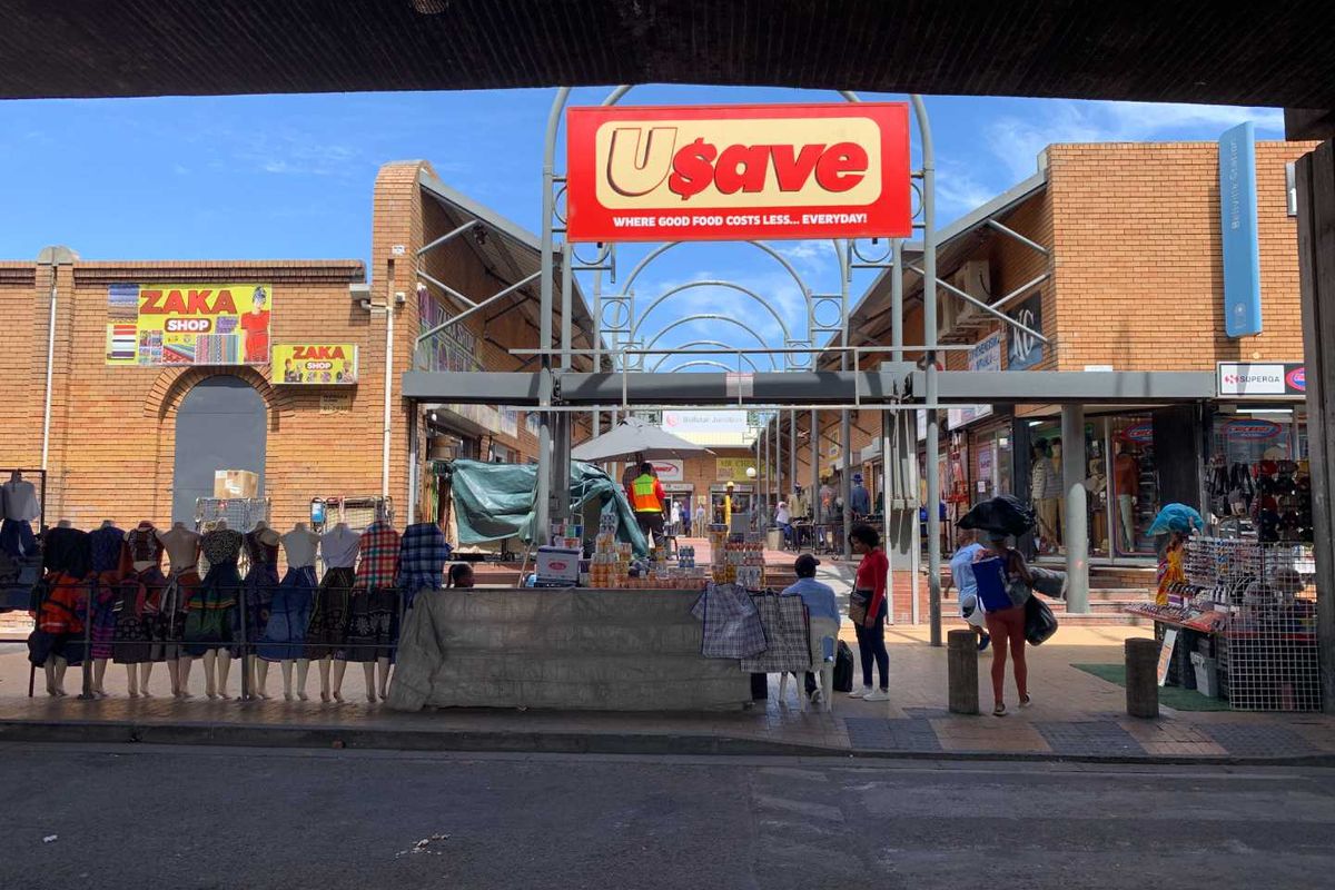 Front view of a retail shopping center entrance featuring brick construction, steel structural elements, and prominent commercial signage.