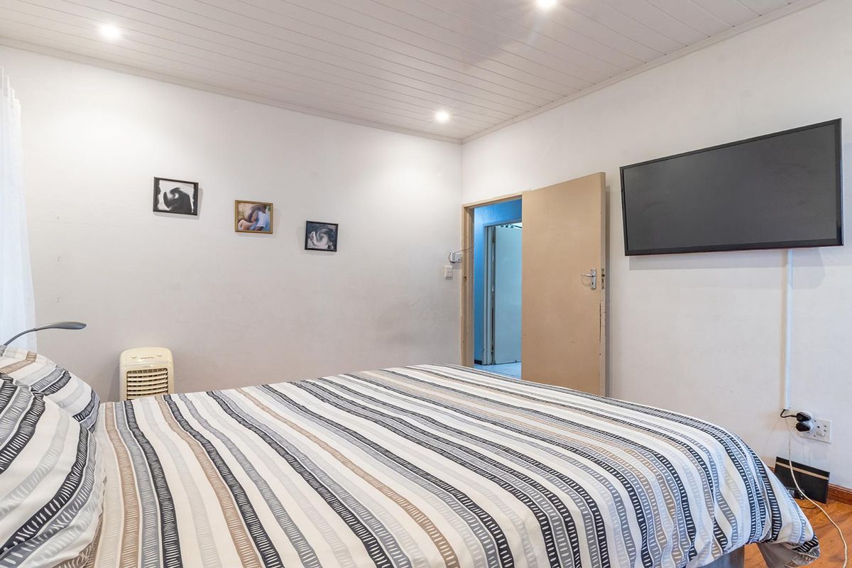 A bedroom featuring timber-look flooring, a tongue and groove ceiling with recessed lighting, and a wall-mounted television.