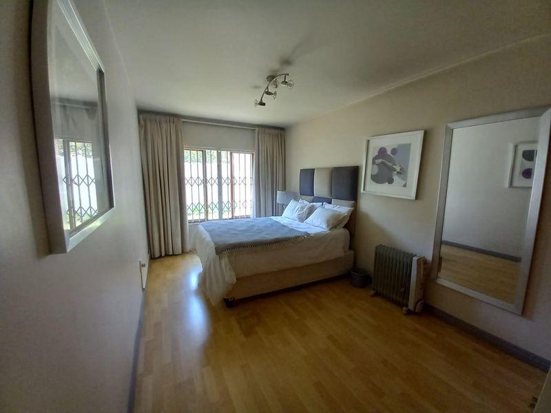 A well-maintained bedroom featuring laminate flooring, a security gate on the window, and neutral wall finishes.