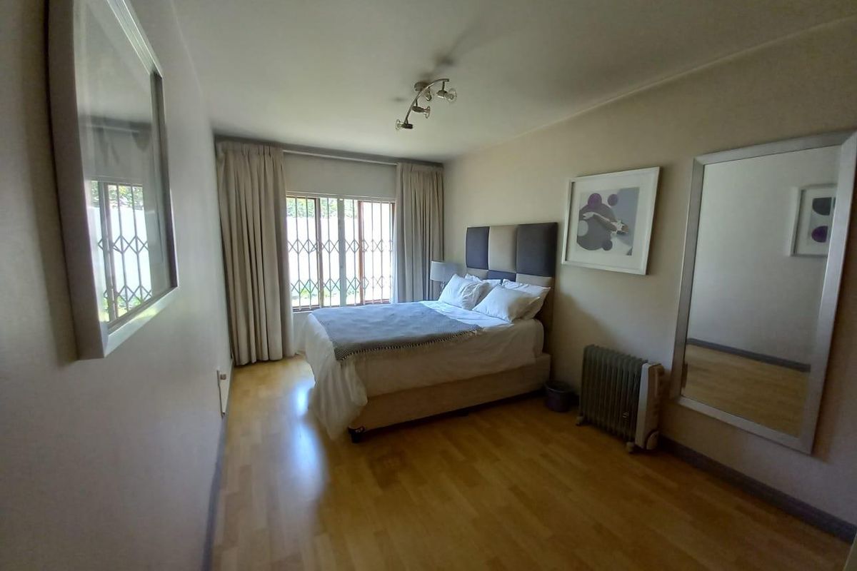 A well-maintained bedroom featuring laminate flooring, a security gate on the window, and neutral wall finishes.