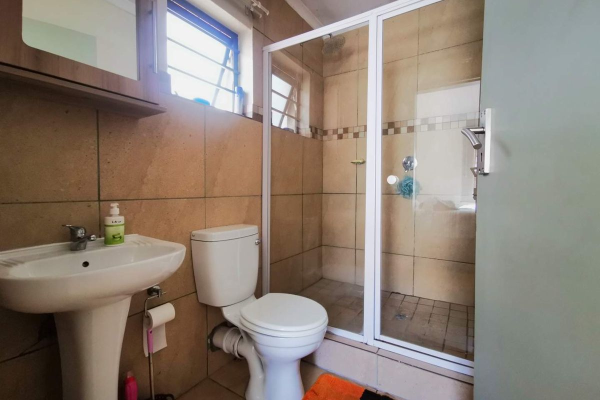 A functional bathroom featuring a pedestal basin, a standard toilet, and a glass-enclosed shower with tiled walls.